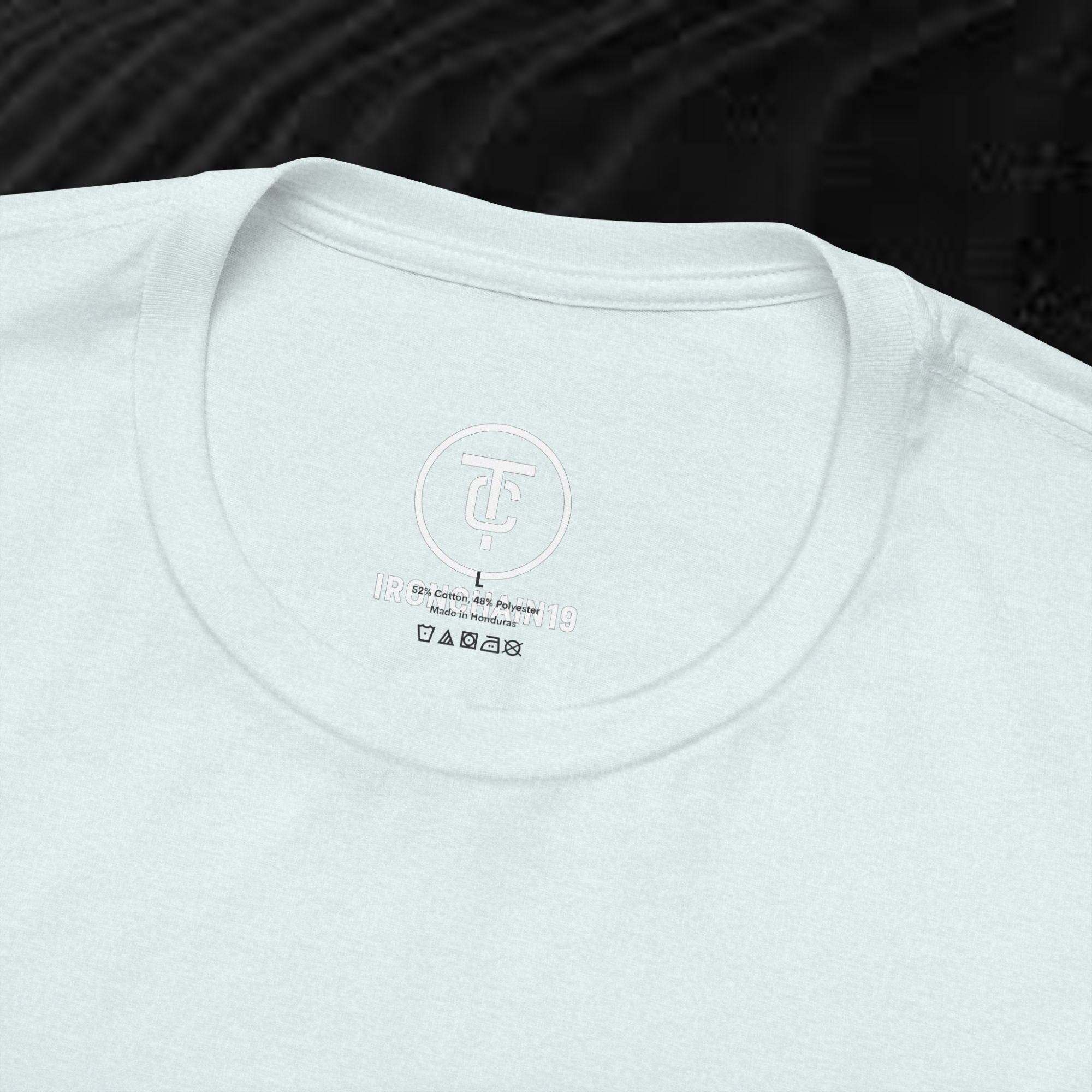 A close-up of the inside collar of a  cotton t-shirt from Ironchain 19. The tagless printed label features a sleek white logo with a chain illustration, surrounded by number19 . Below the logo, the text indicates the shirt is 100% cotton, made in Bangladesh, and includes washing care symbols. The soft fabric and seamless neckline highlight the premium quality and comfort of this Gothic aesthetics  perfect for cat lovers and fans of modern streetwear fashion.