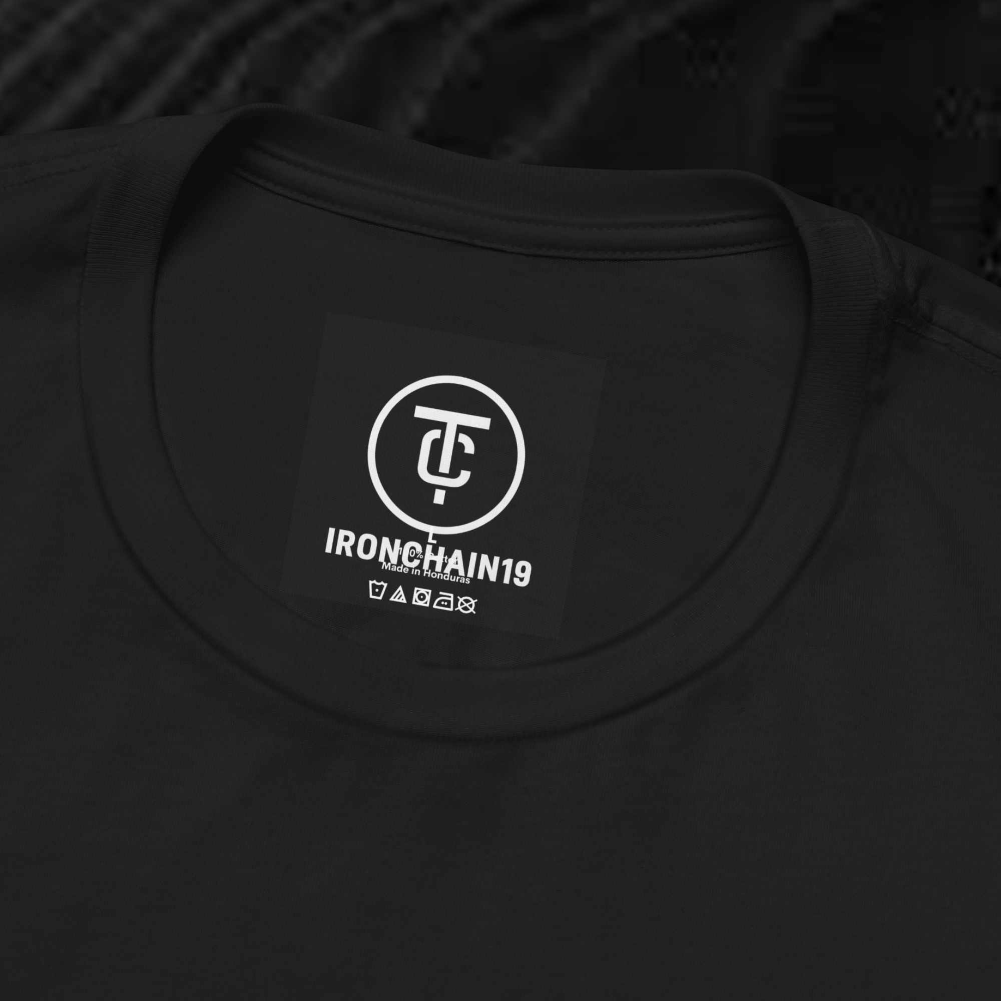 A close-up of the inside collar of a  cotton t-shirt from Ironchain 19. The tagless printed label features a sleek white logo with a chain illustration, surrounded by number19 . Below the logo, the text indicates the shirt is 100% cotton, made in Bangladesh, and includes washing care symbols. The soft fabric and seamless neckline highlight the premium quality and comfort of this Gothic aesthetics  perfect for cat lovers and fans of modern streetwear fashion.