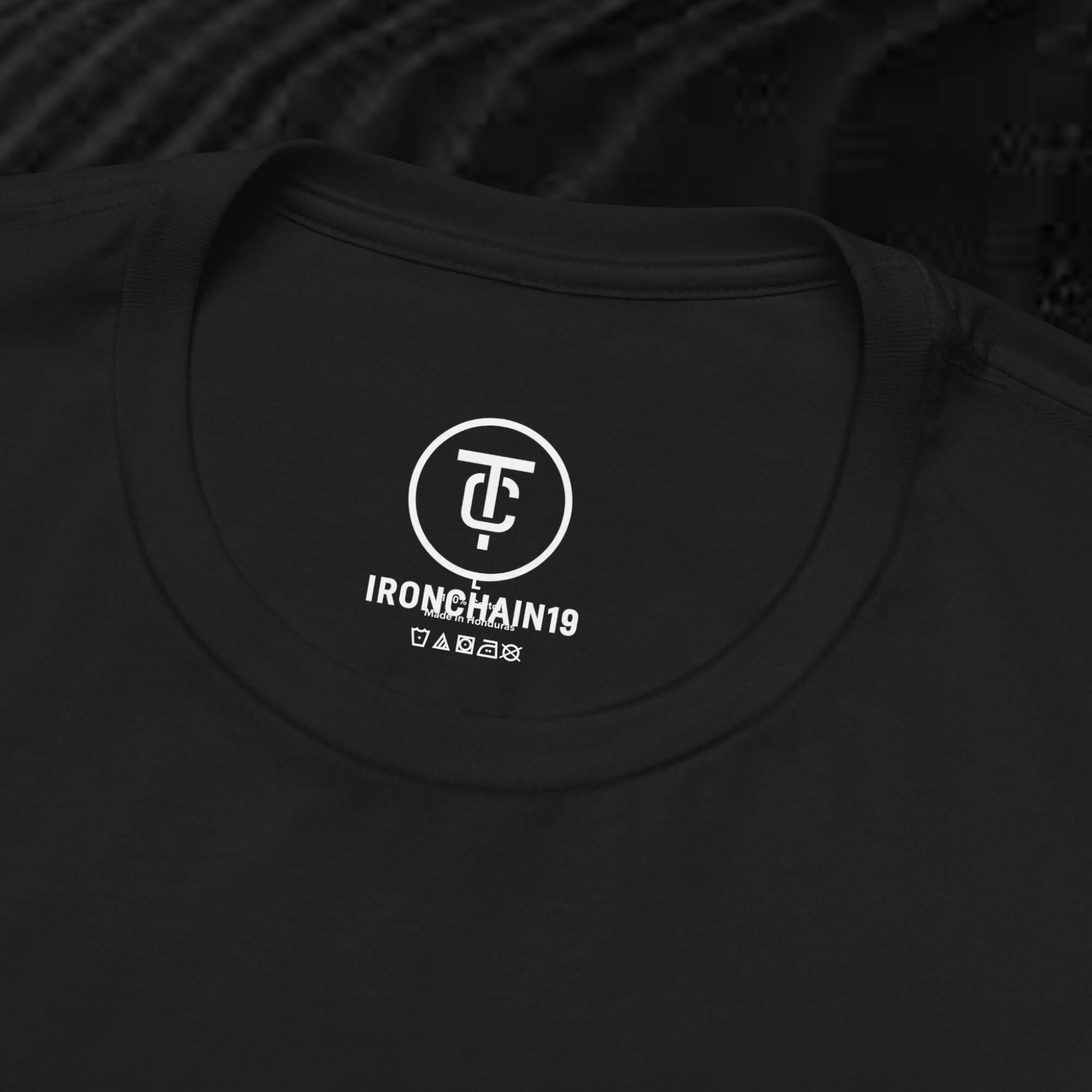 A close-up of the inside collar of a  cotton t-shirt from Ironchain 19. The tagless printed label features a sleek white logo with a chain illustration, surrounded by number19 . Below the logo, the text indicates the shirt is 100% cotton, made in Bangladesh, and includes washing care symbols. The soft fabric and seamless neckline highlight the premium quality and comfort of this Gothic aesthetics  perfect for cat lovers and fans of modern streetwear fashion.