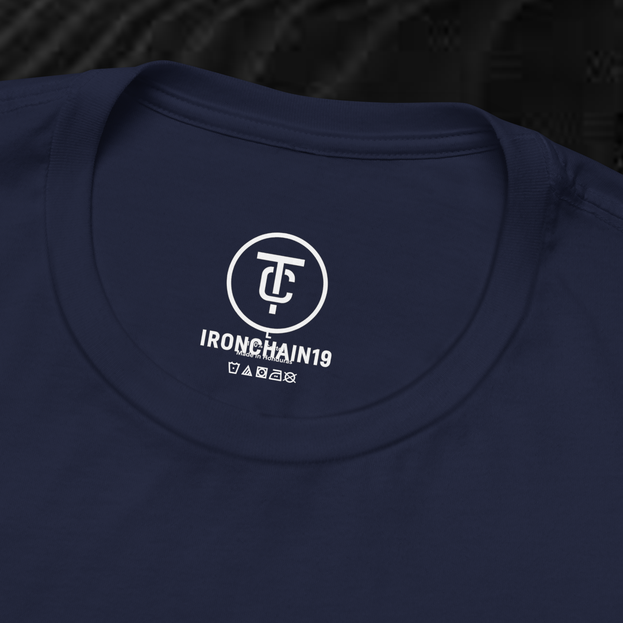 A close-up of the inside collar of a  cotton t-shirt from Ironchain 19. The tagless printed label features a sleek white logo with a chain illustration, surrounded by number19 . Below the logo, the text indicates the shirt is 100% cotton, made in Bangladesh, and includes washing care symbols. The soft fabric and seamless neckline highlight the premium quality and comfort of this Gothic aesthetics  perfect for cat lovers and fans of modern streetwear fashion.